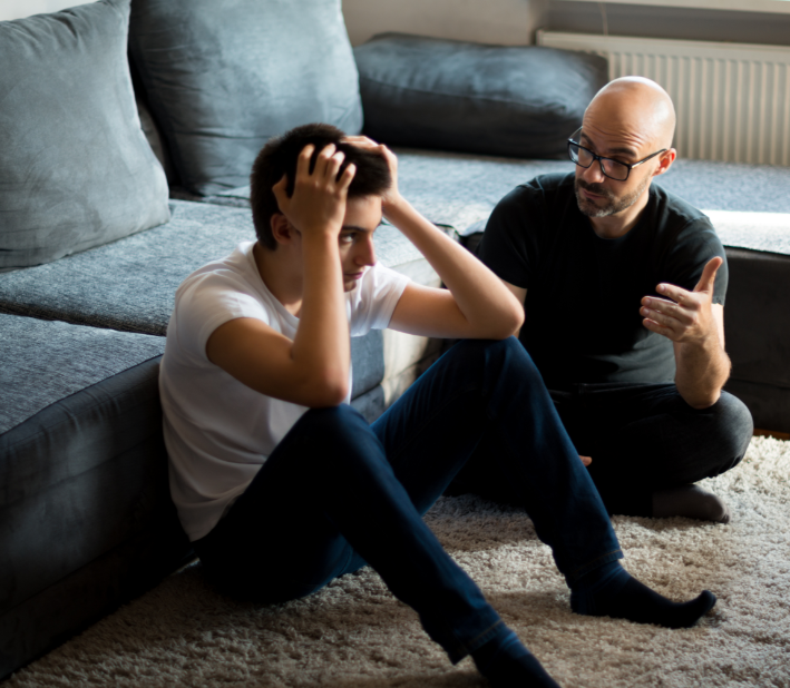 A man is talking to a young man who is sitting on the floor