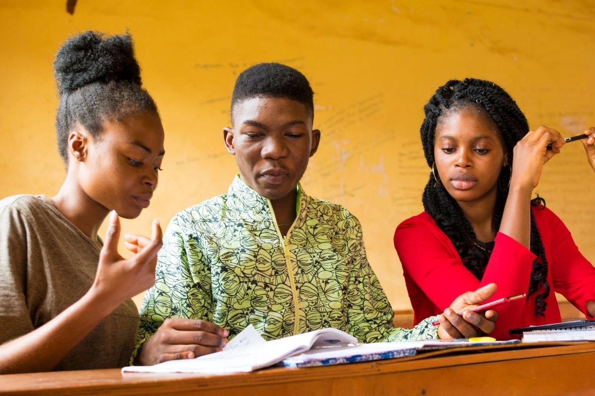 A group of young people are sitting at a desk in a classroom.