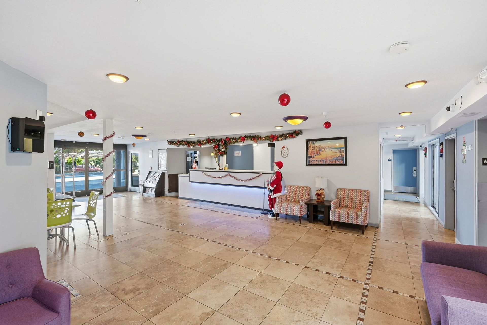 Bright hotel lobby with tiled floors, reception desk, festive decorations, and several chairs.