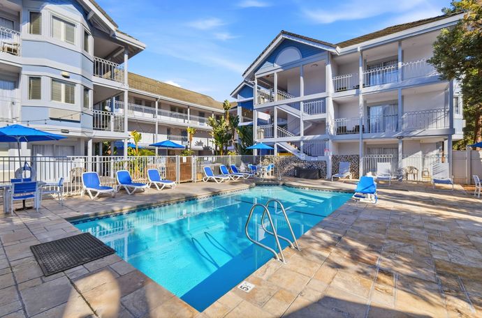 Outdoor swimming pool surrounded by a stone deck and lounge chairs between blue multi-story apartment buildings.