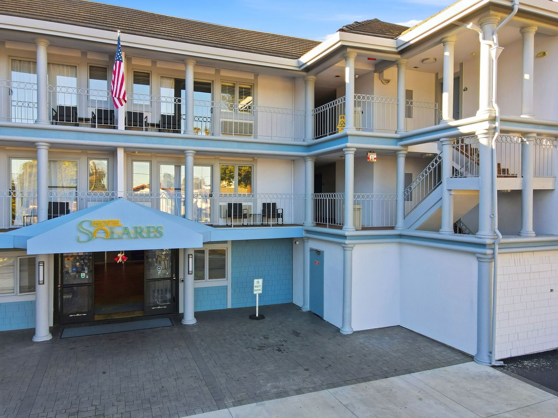 A two-story hotel building with a blue awning, white pillars, balconies, and an American flag flying out front.