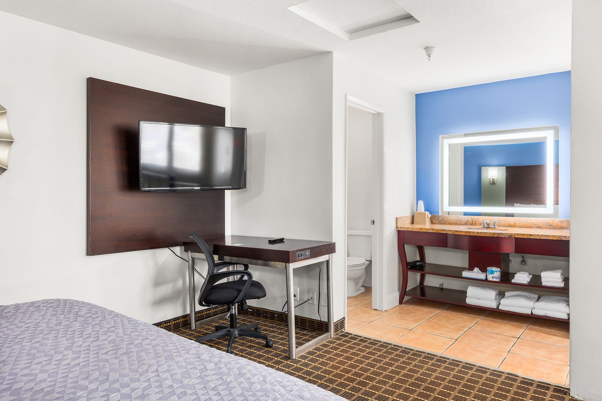 Hotel room featuring a flat-screen TV, desk with a chair, and an open bathroom with a vanity and vanity mirror.