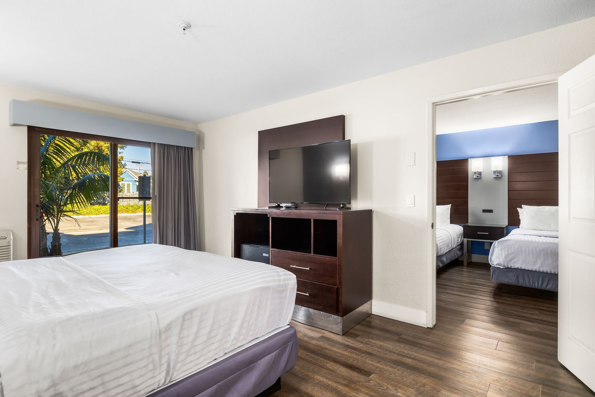 A hotel suite featuring a king bed in the foreground and an adjoining room with two beds visible through an open doorway.
