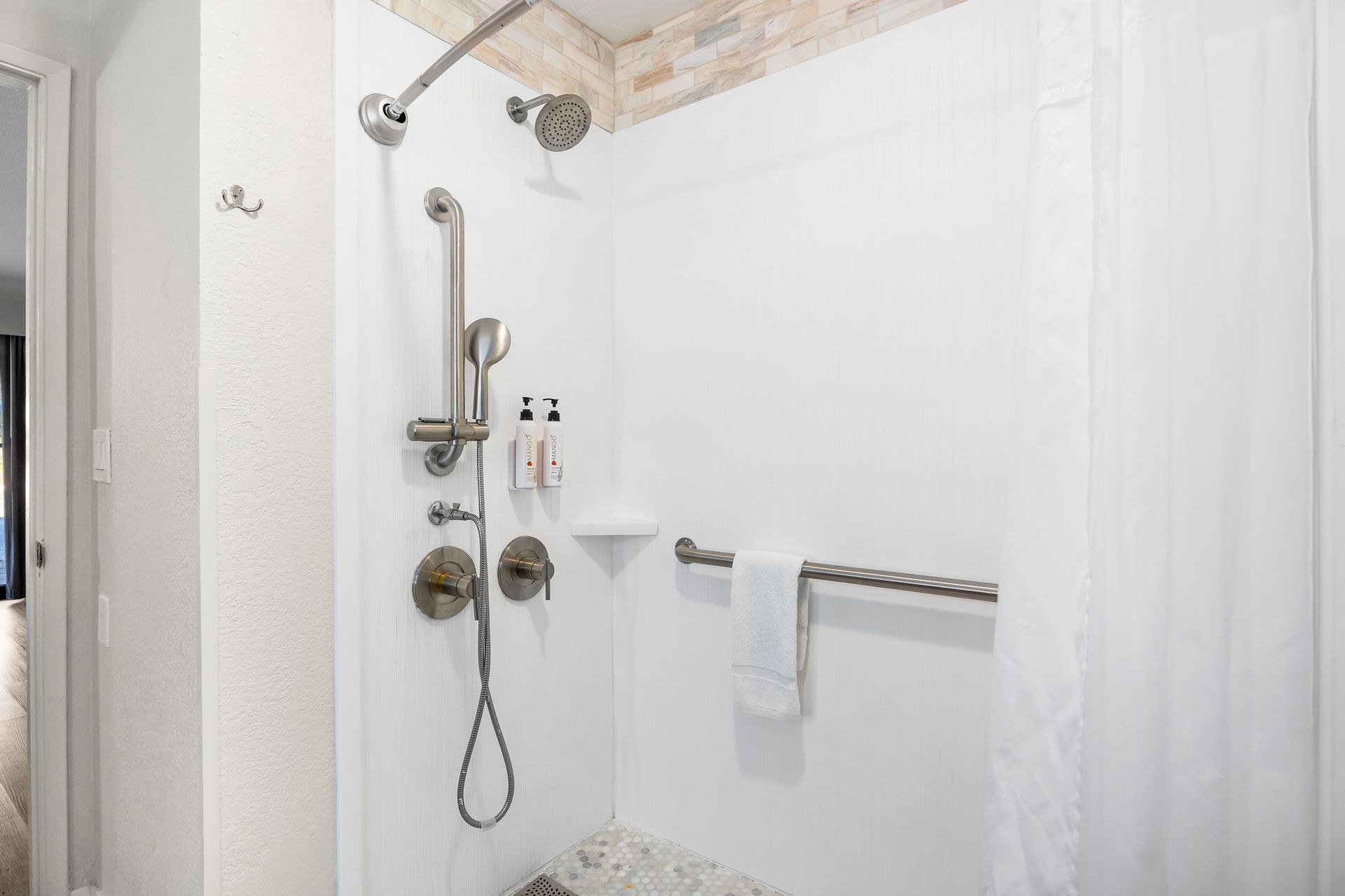 An accessible walk-in shower with a white surround, grab bars, a handheld showerhead, and a towel hanging on the wall.
