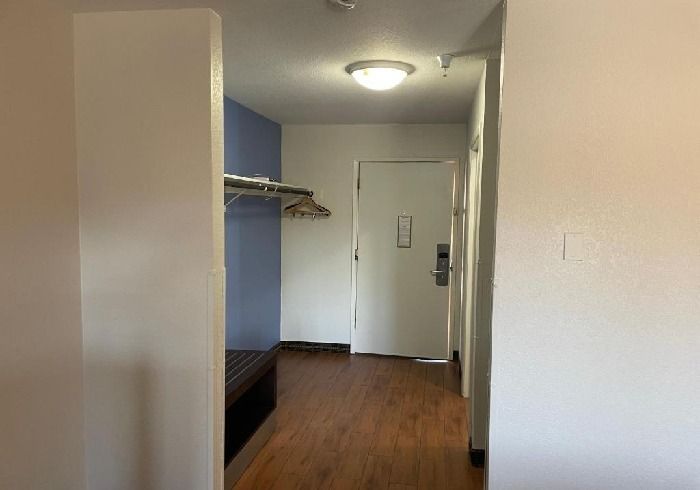A hotel room entryway with wood-look flooring, a blue accent wall, a clothing rack, a bench, and a white entrance door.
