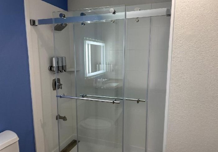 Modern walk-in shower with clear glass sliding doors and silver hardware against a white tile wall and a blue painted wall.