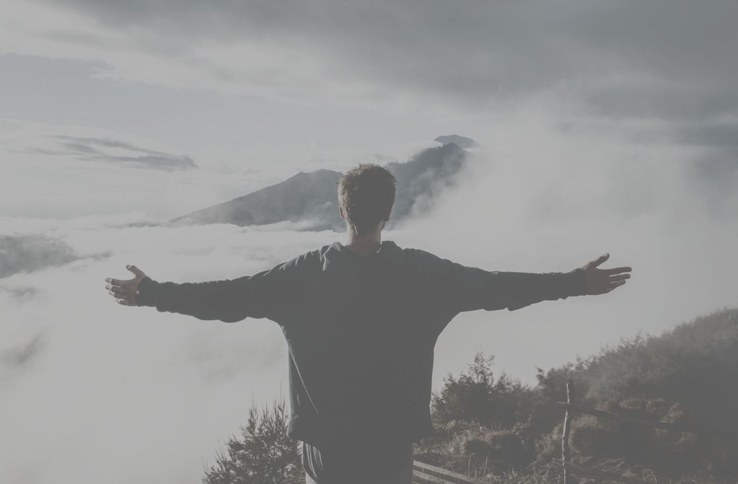 A man is standing on top of a mountain with his arms outstretched.