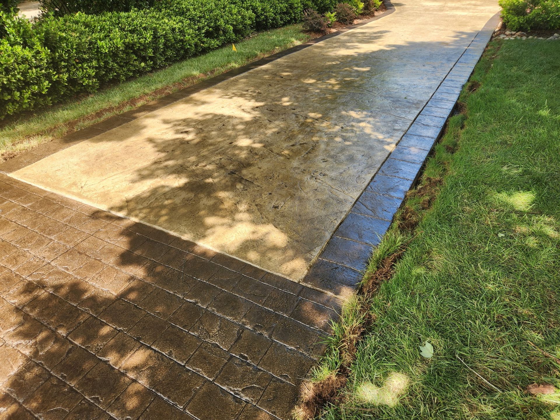 Wet concrete pathway and textured brick border with green grass and hedge.