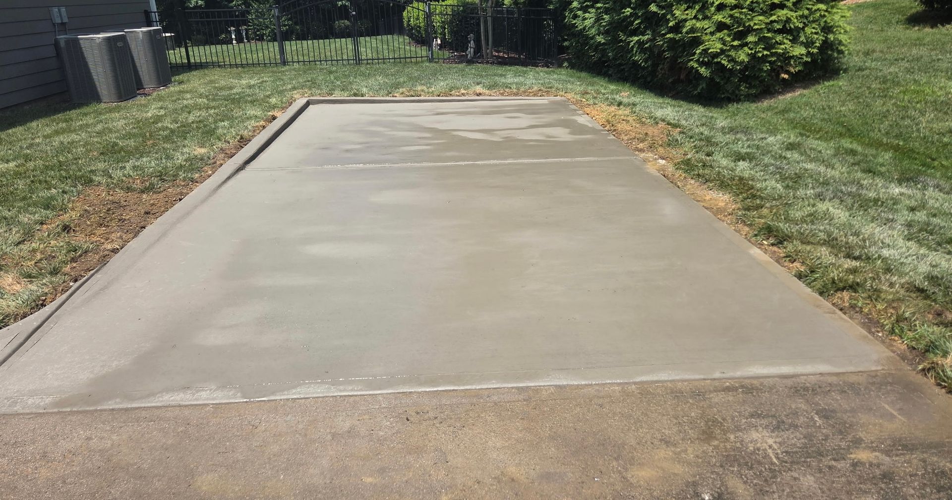Newly poured gray concrete patio in a grassy yard.