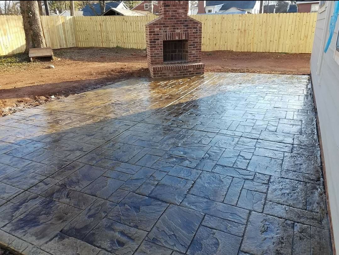 Brick fireplace on stamped concrete patio, wet with water, in a backyard with a wooden fence.