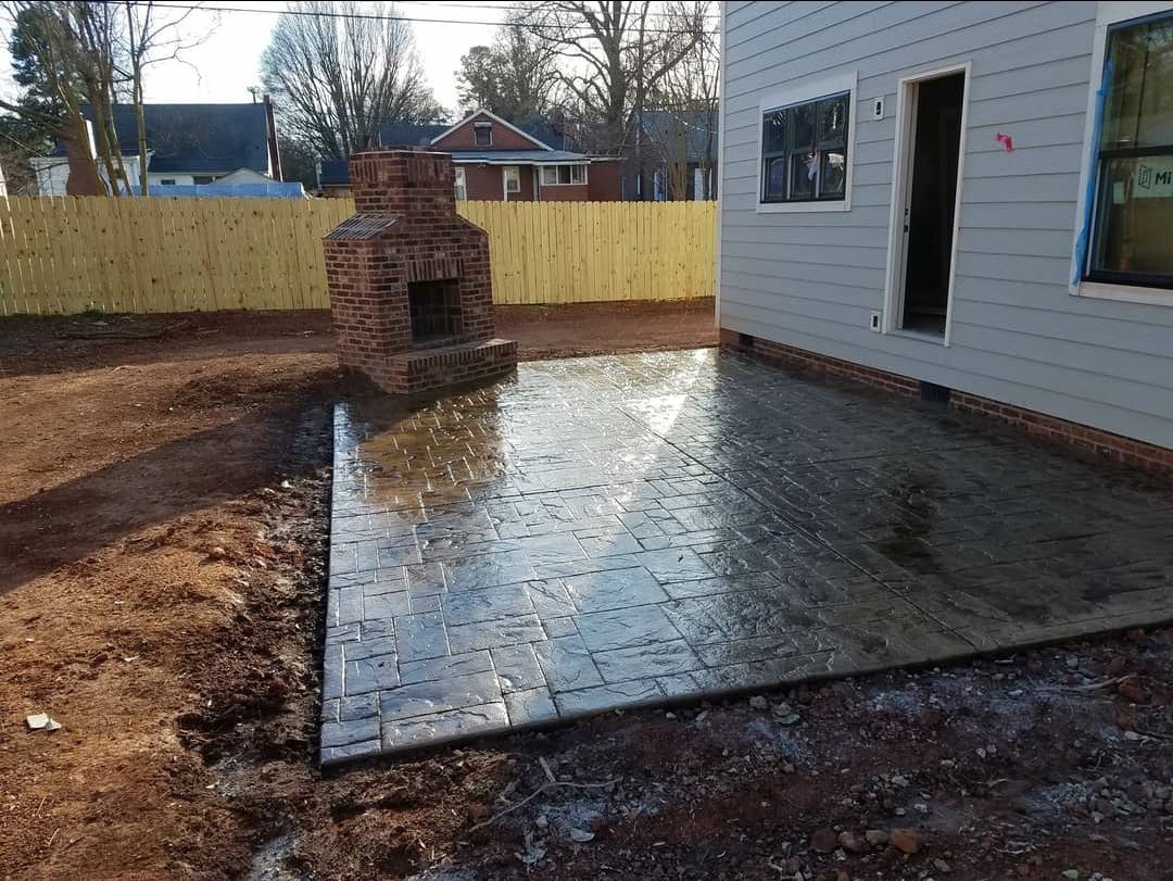 Brick patio with fireplace, next to house, in front of yellow fence.