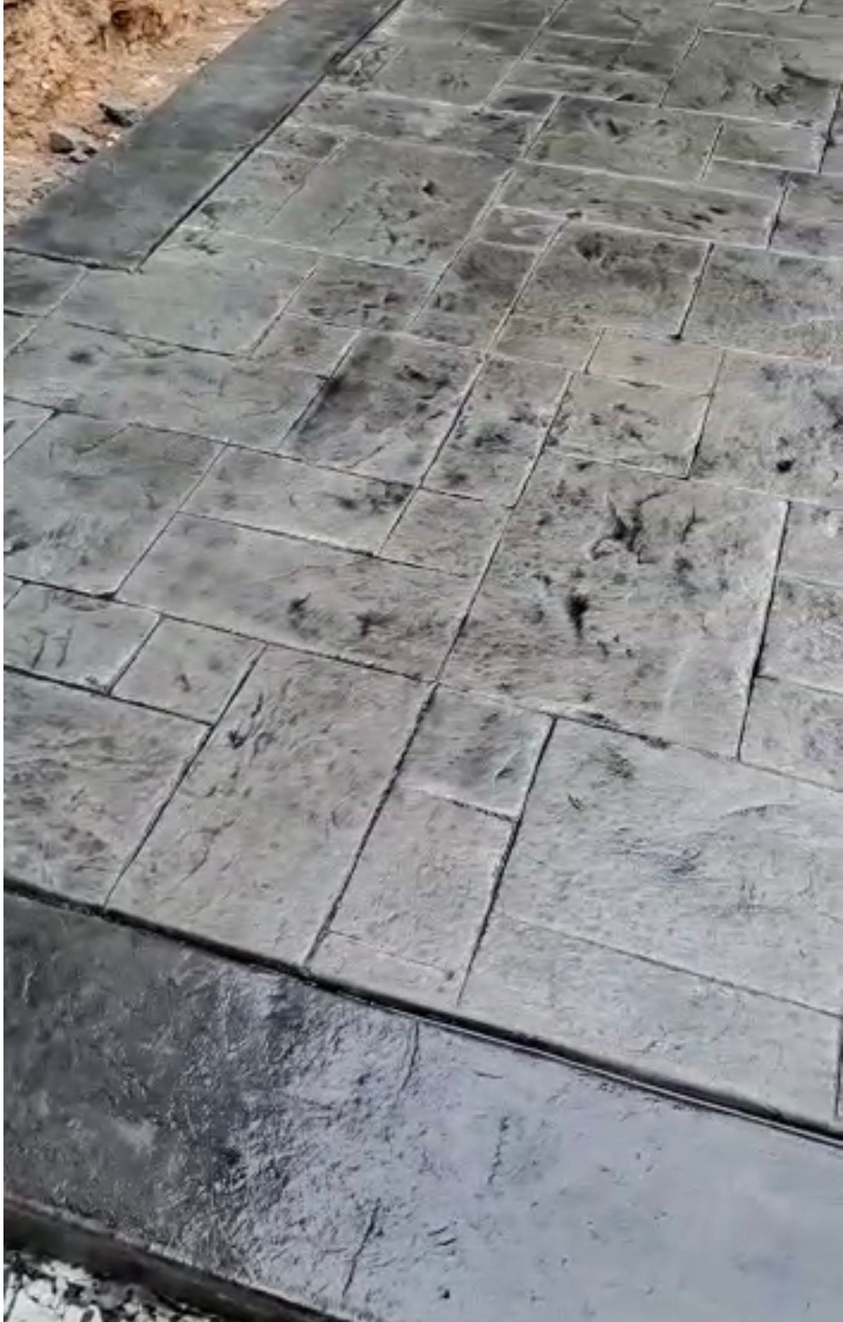 Textured gray concrete patio with darker border, resembling a brick pattern.