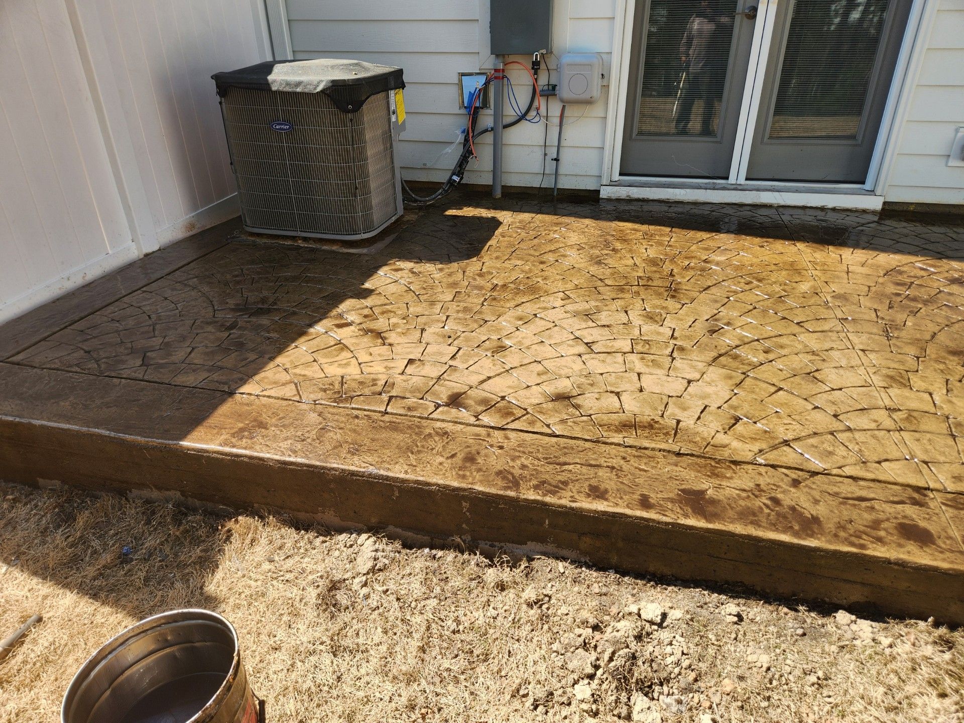 Stamped concrete patio next to a house with air conditioning unit and gravel.