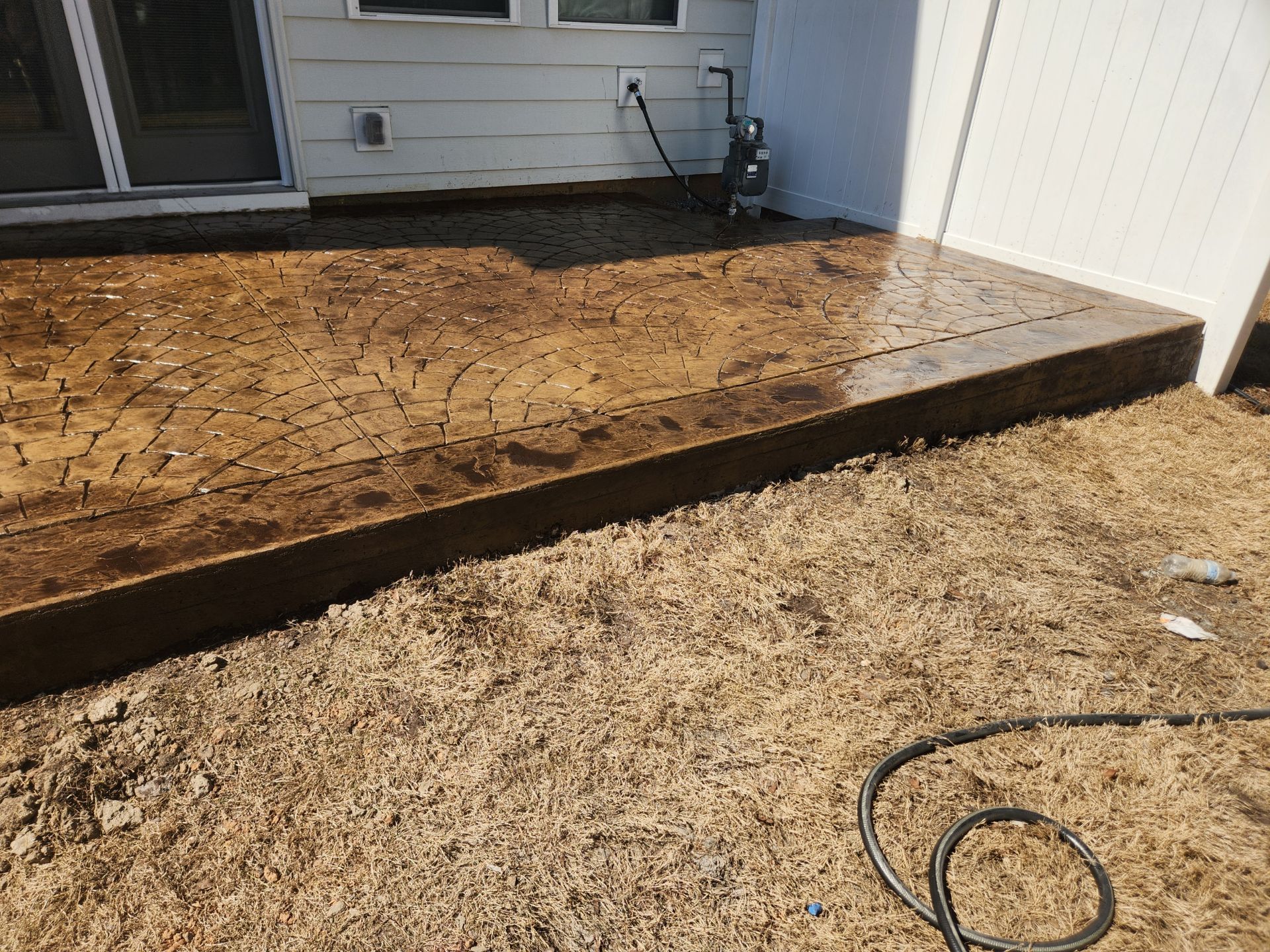 Brown stamped concrete patio next to gravel and a white fence.