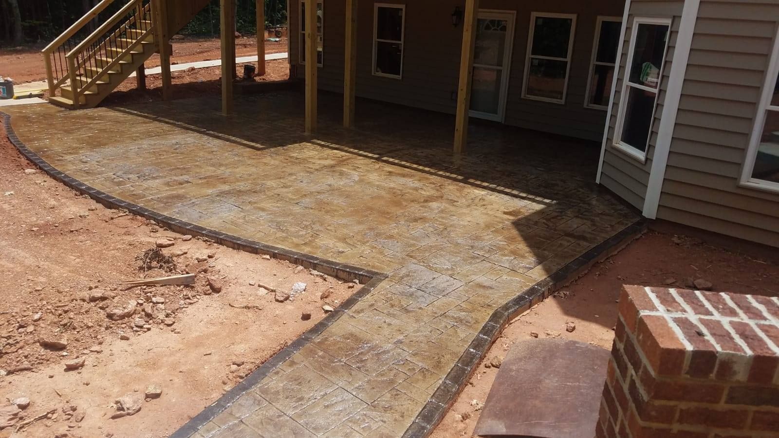 A new concrete walkway and patio next to a house and brick feature, surrounded by dirt.