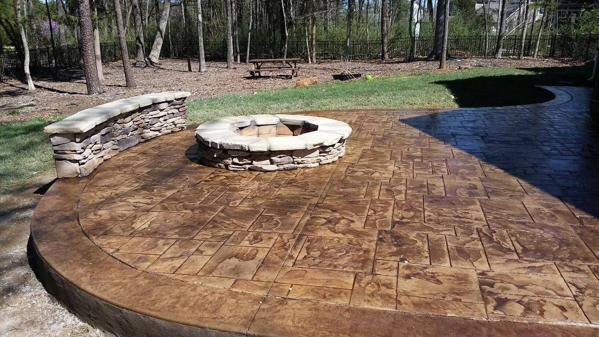 Stamped concrete patio with fire pit and stone bench in a backyard.