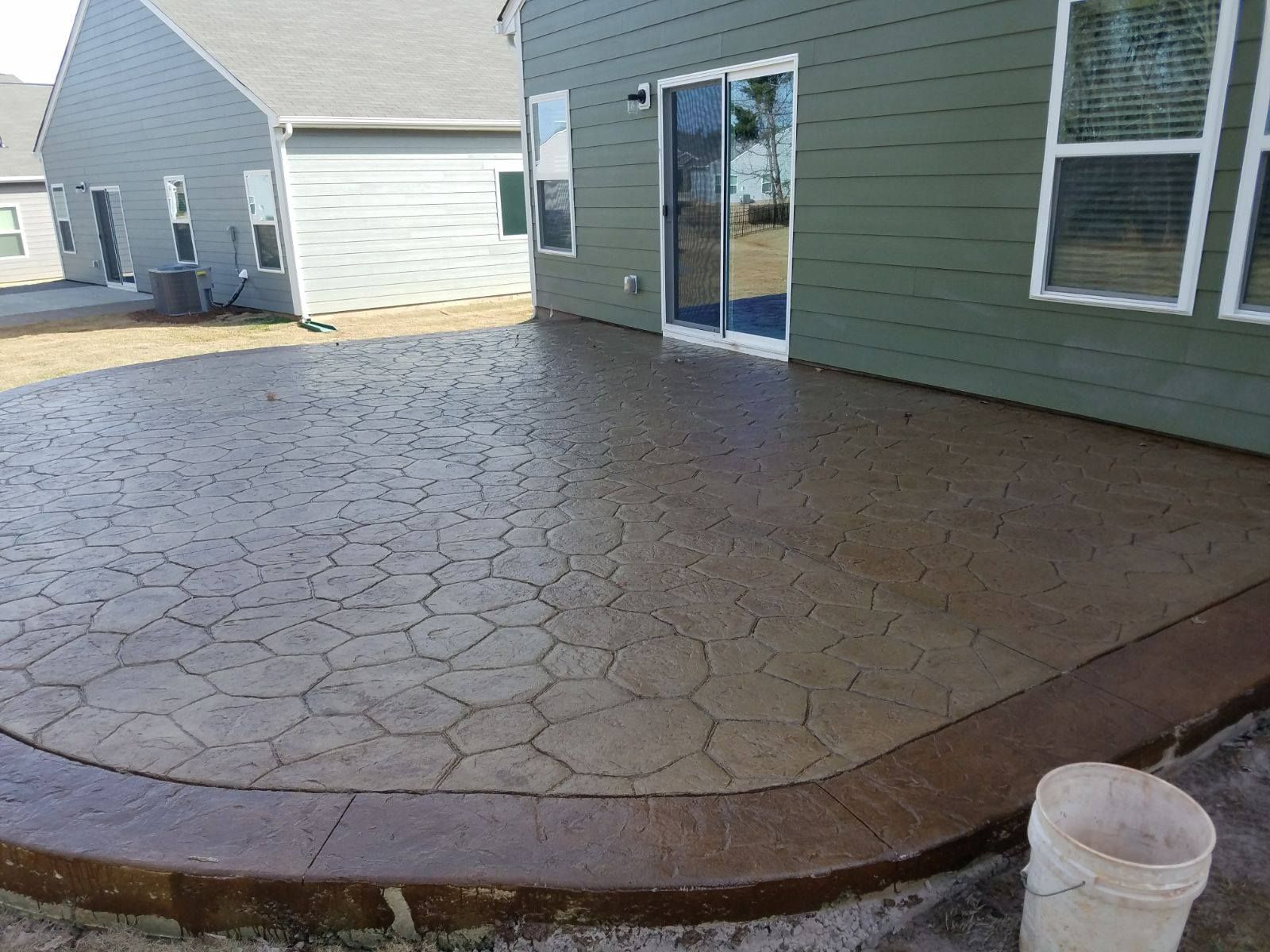 Concrete patio with patterned design, brown border, next to a house with sliding glass door.