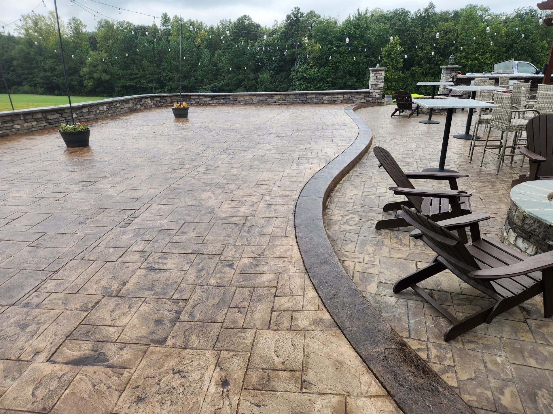 Outdoor patio with stamped concrete, wooden chairs, and tables, under an overcast sky.
