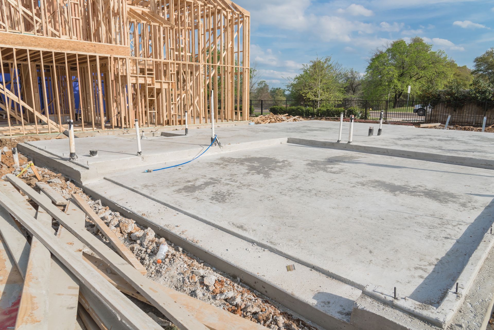 Construction site: wooden frame of a house, concrete foundation, plumbing visible.