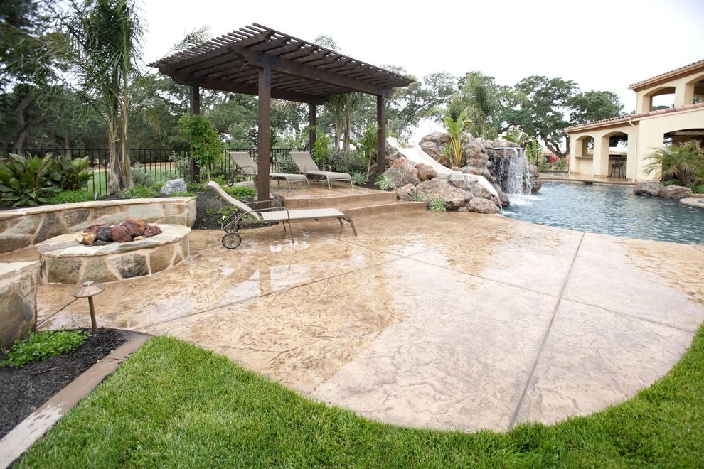 Patio with fire pit, pergola, pool, and waterfall in a backyard setting.