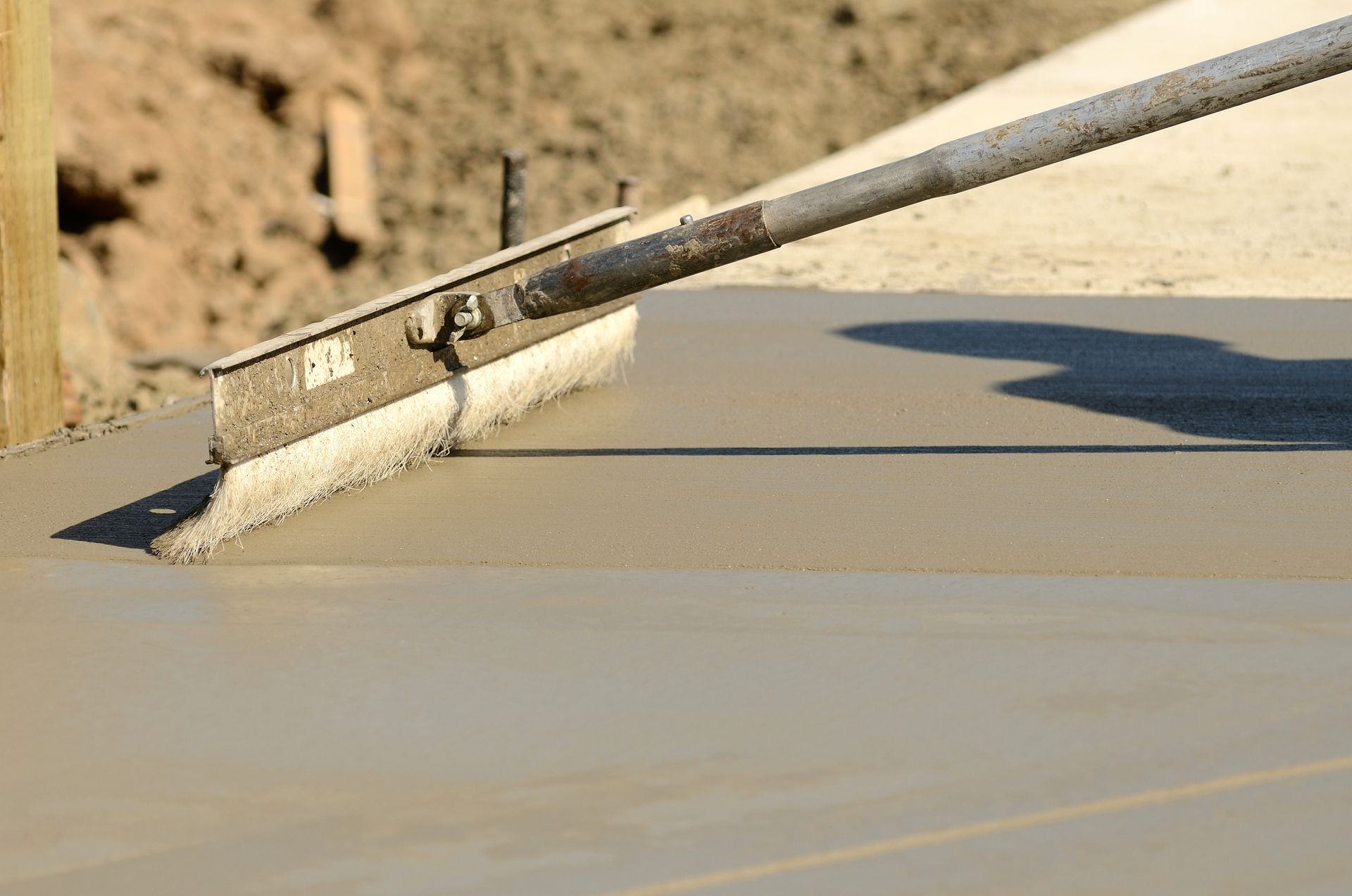 A concrete worker using a brush to smooth fresh concrete.