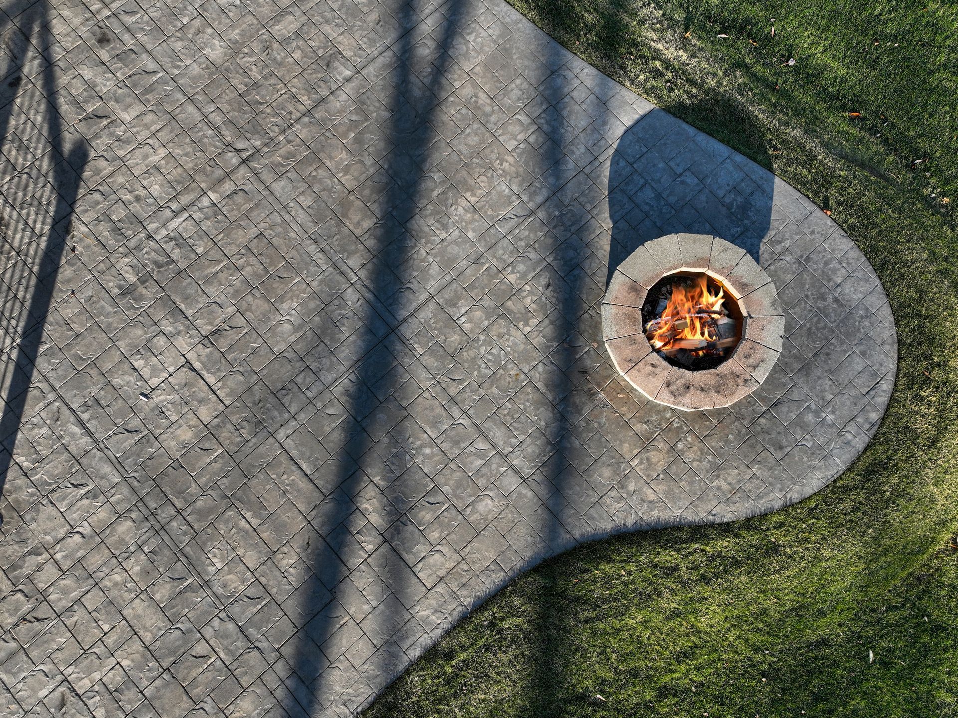 Overhead view of brick patio with a fire pit, and surrounding grass.
