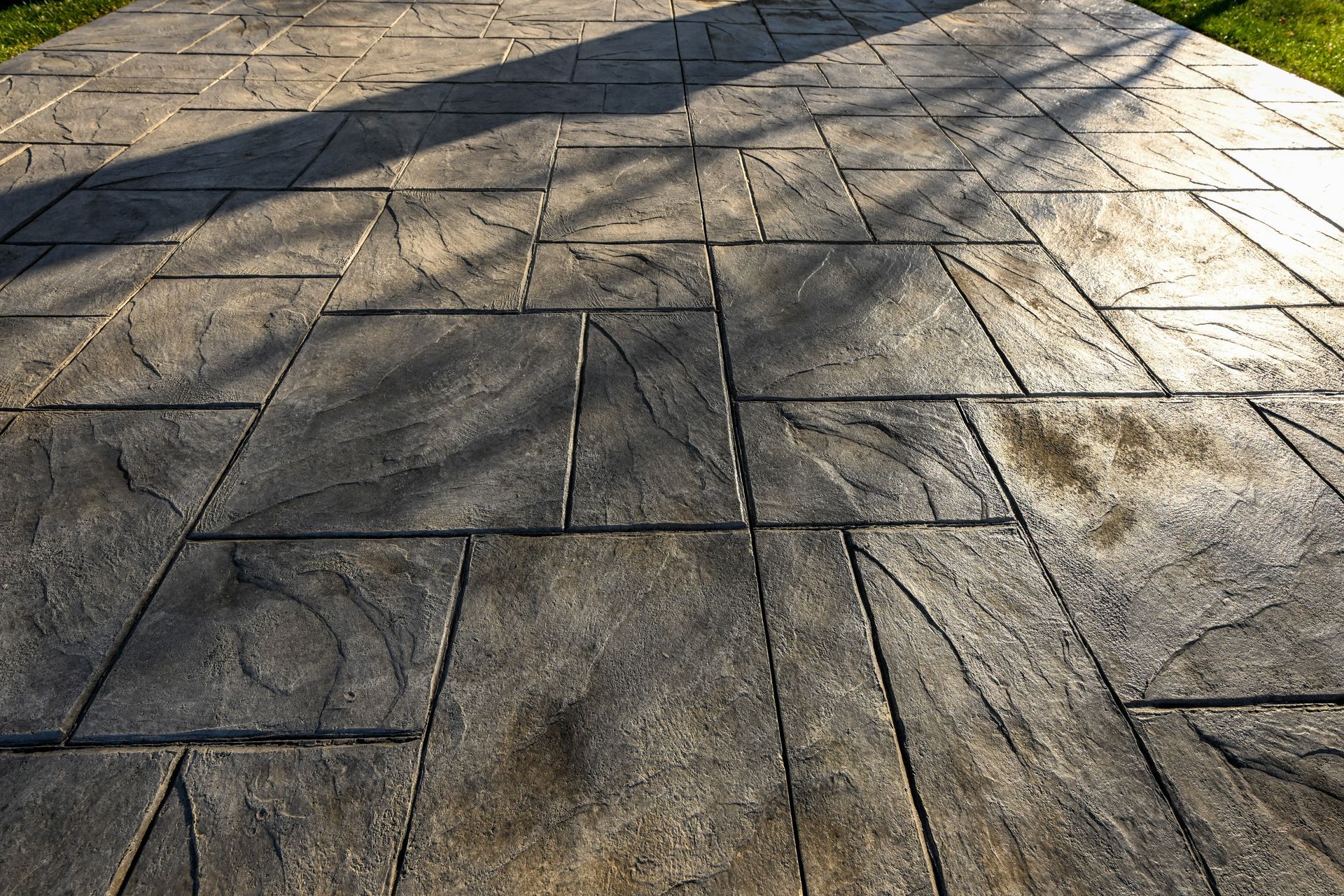 Stamped concrete walkway with gray stone pattern, lit by sunlight with shadows.