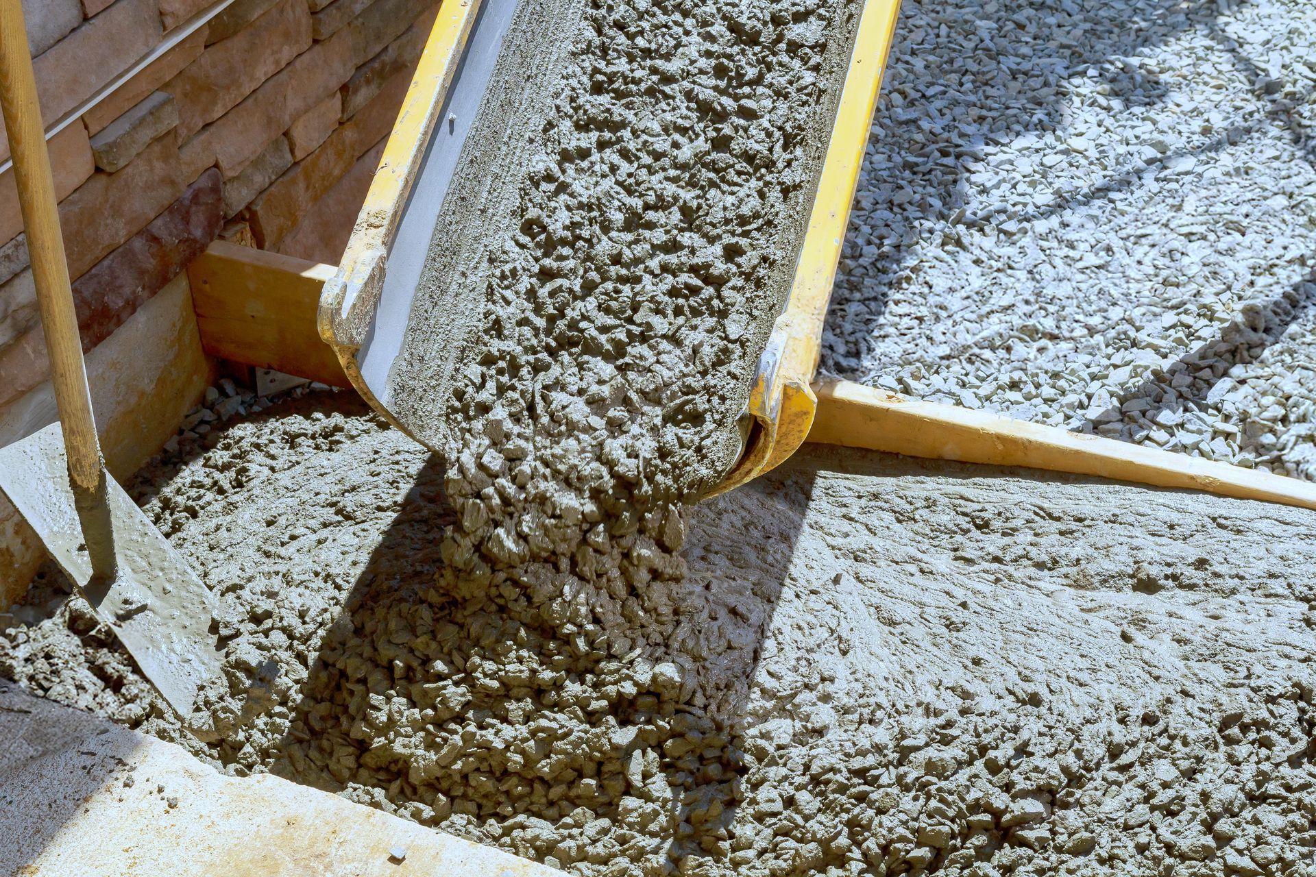 Concrete being poured from a chute into a form, next to a brick wall and a wooden board.