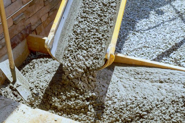 Concrete being poured from a chute into a form, next to a brick wall and a wooden board.