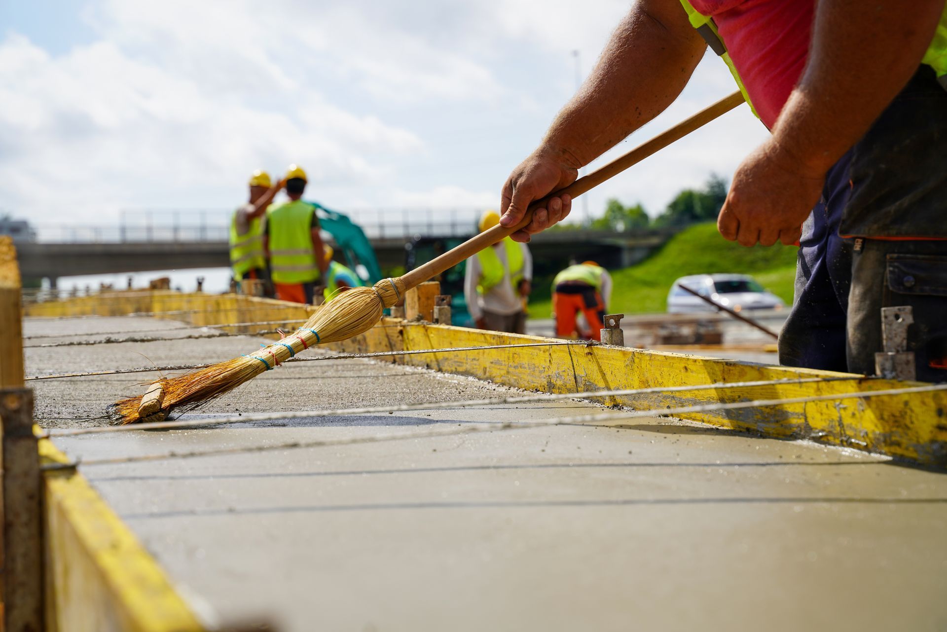 Construction worker leveling wet concrete with a long tool on a bright day.