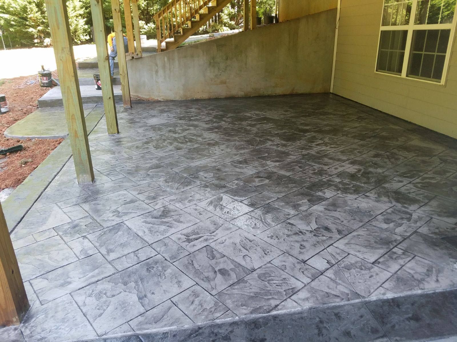 Concrete patio with stamped tile pattern, gray color, beneath a wooden structure.