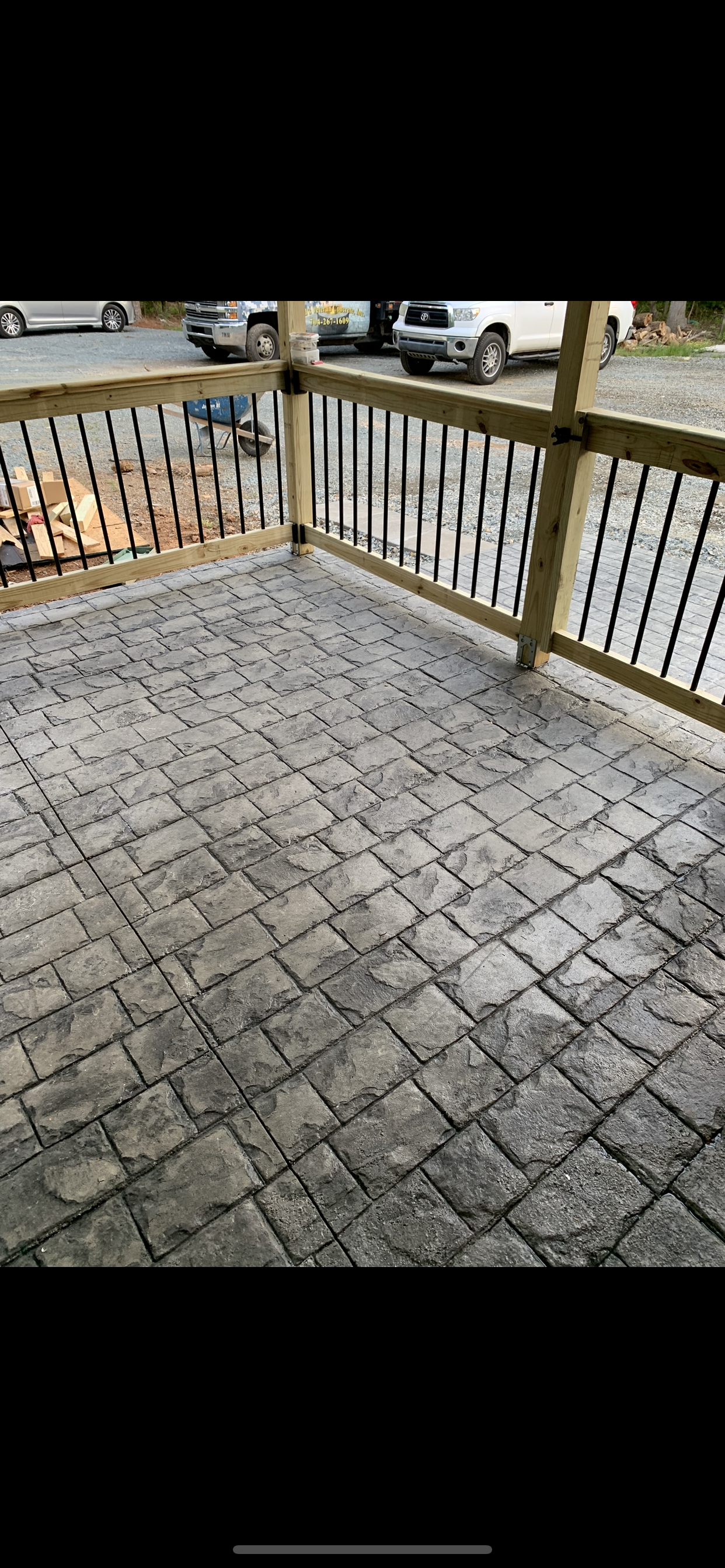 A deck with gray stone pavers, wood railings, and a black metal fence.