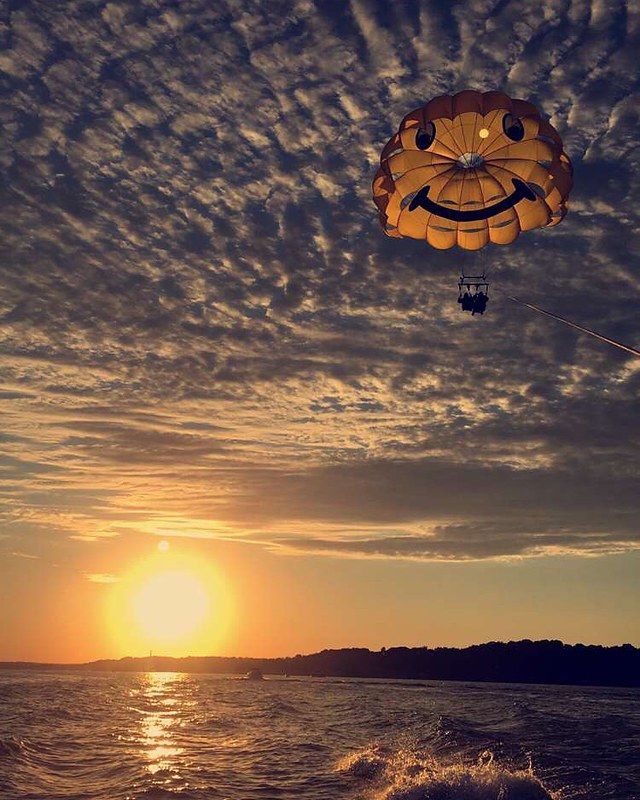 Parasailing over a sunset ocean, with orange sky, clouds, and sparkling water.