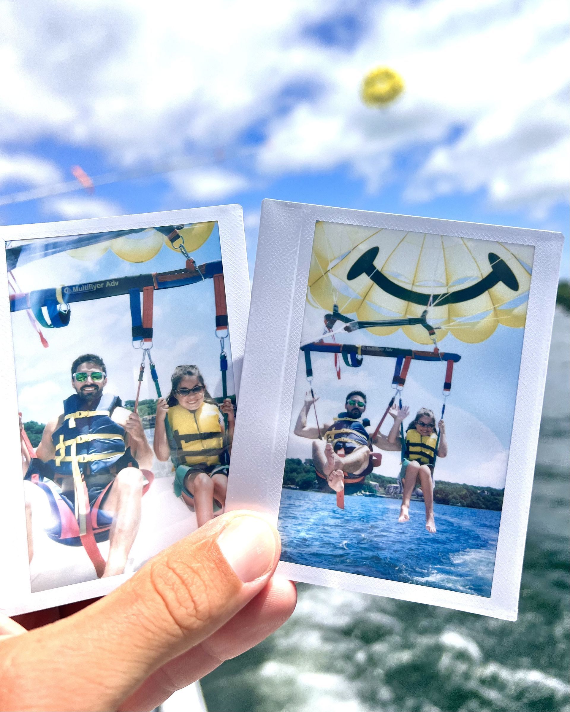 Hand holding two parasailing photos against a sunny blue sea and sky
