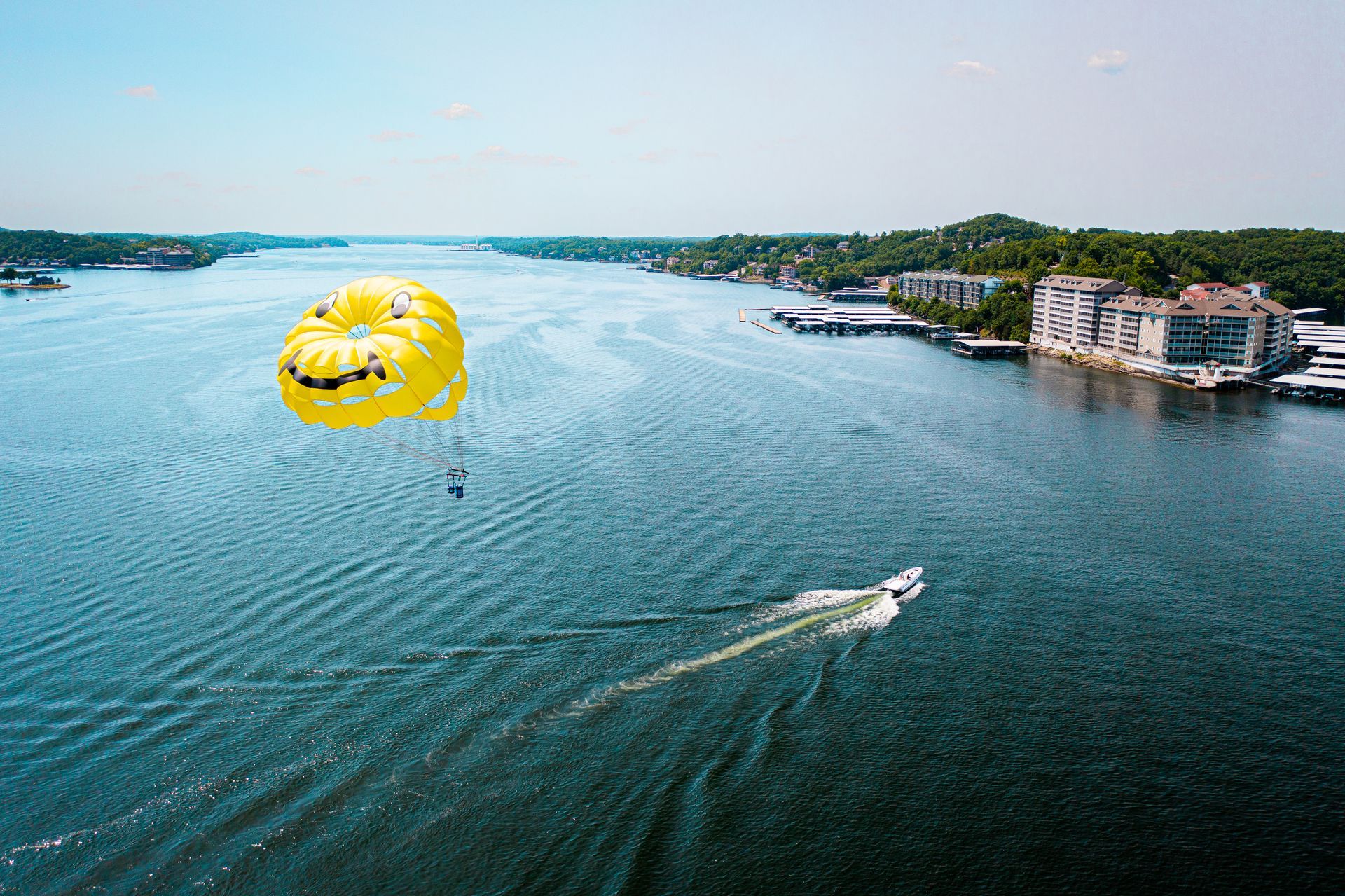 Yellow parasail towing a speedboat across blue water near a rocky shoreline