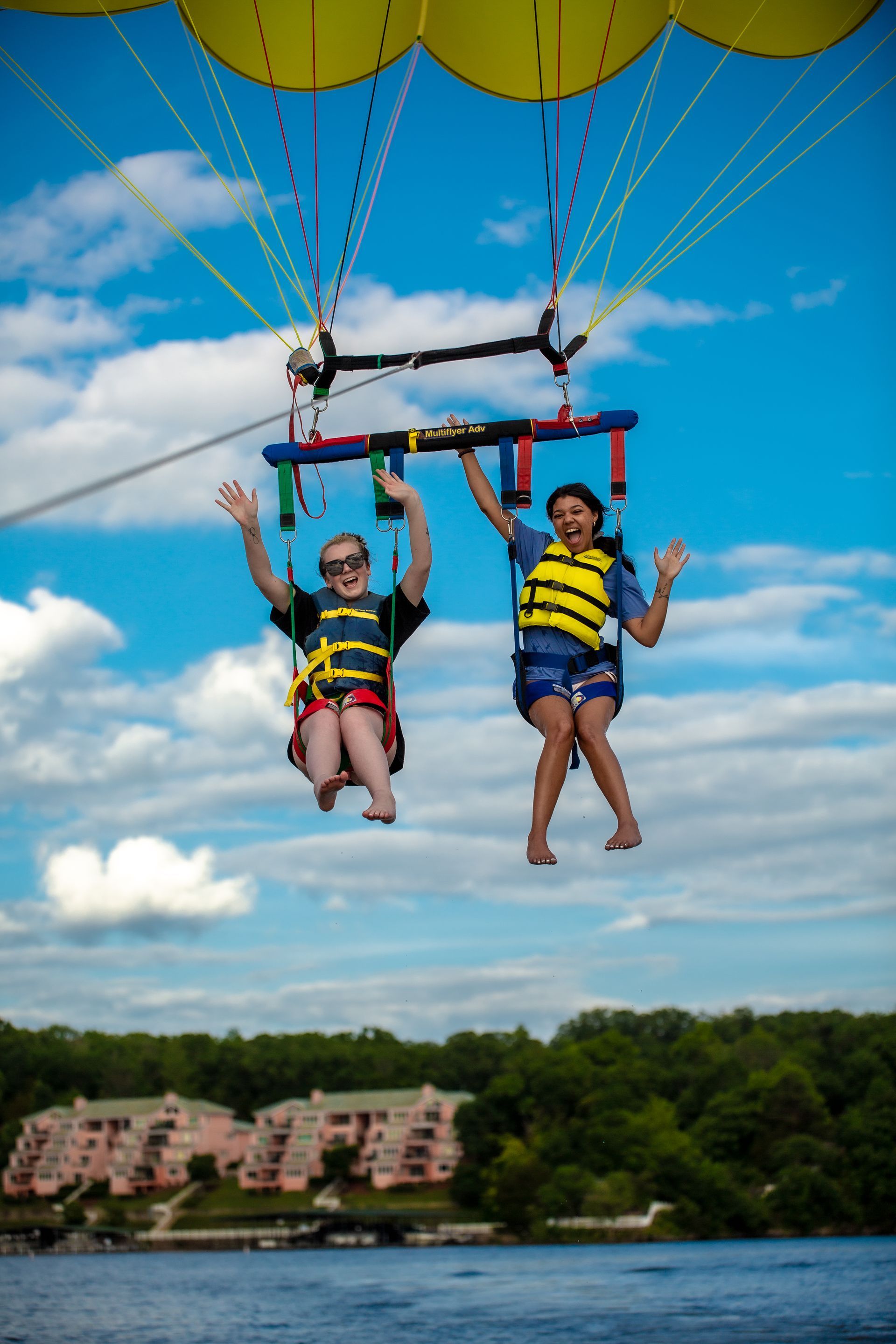 Two people parasailing above water under a blue sky, wearing life jackets and harnesses