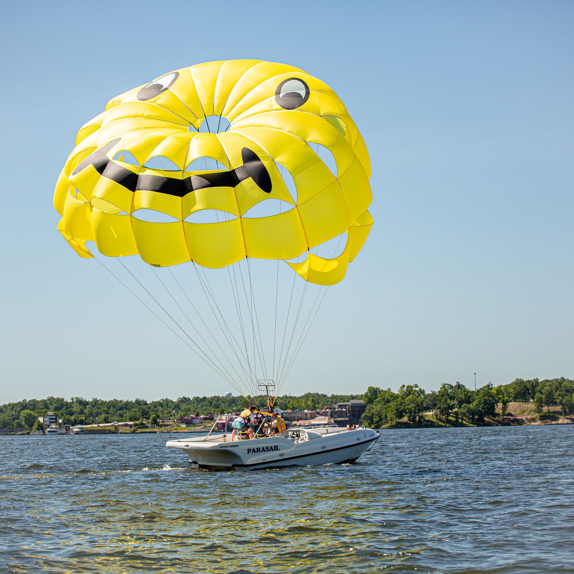 Yellow parasail with a smiley face towing a boat over choppy water near a shoreline
