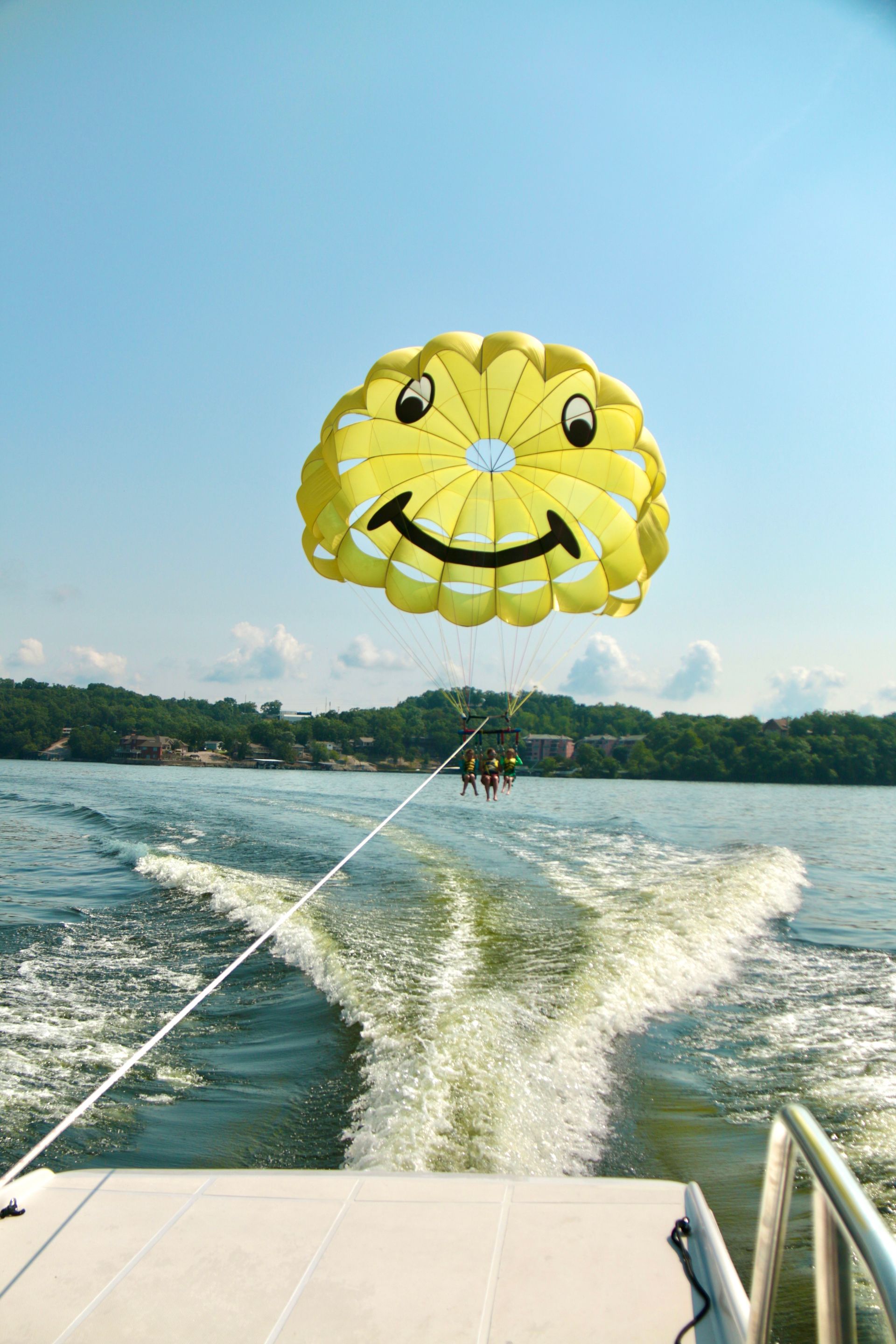 Yellow smiley-face parasail above a lake, towed behind a boat leaving a foamy wake