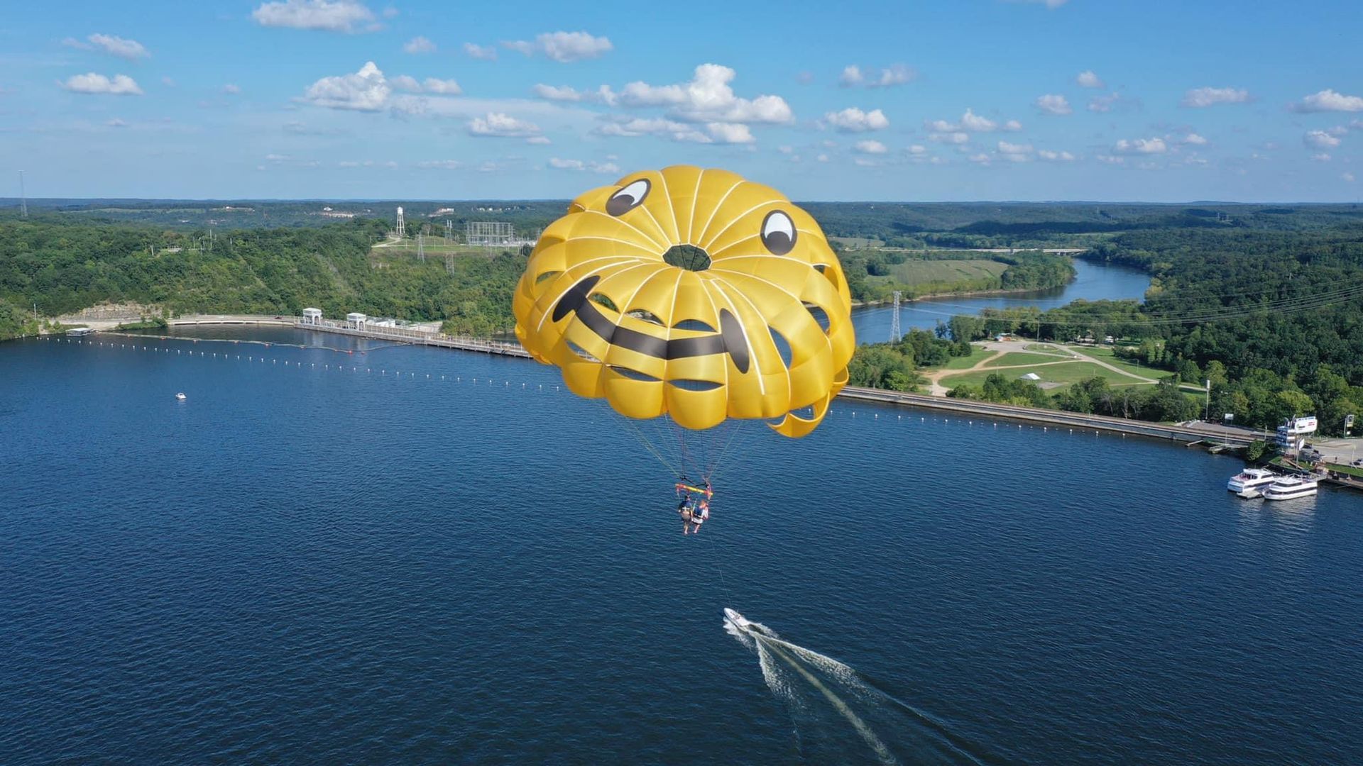 Yellow parachute canopy over a blue lake with a speedboat trailing below on a sunny day