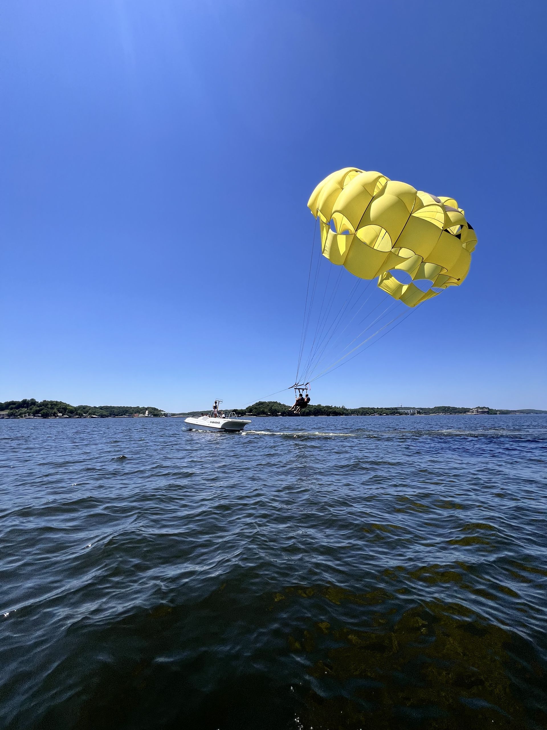 Yellow parasail over choppy blue water with a boat below under a clear sky