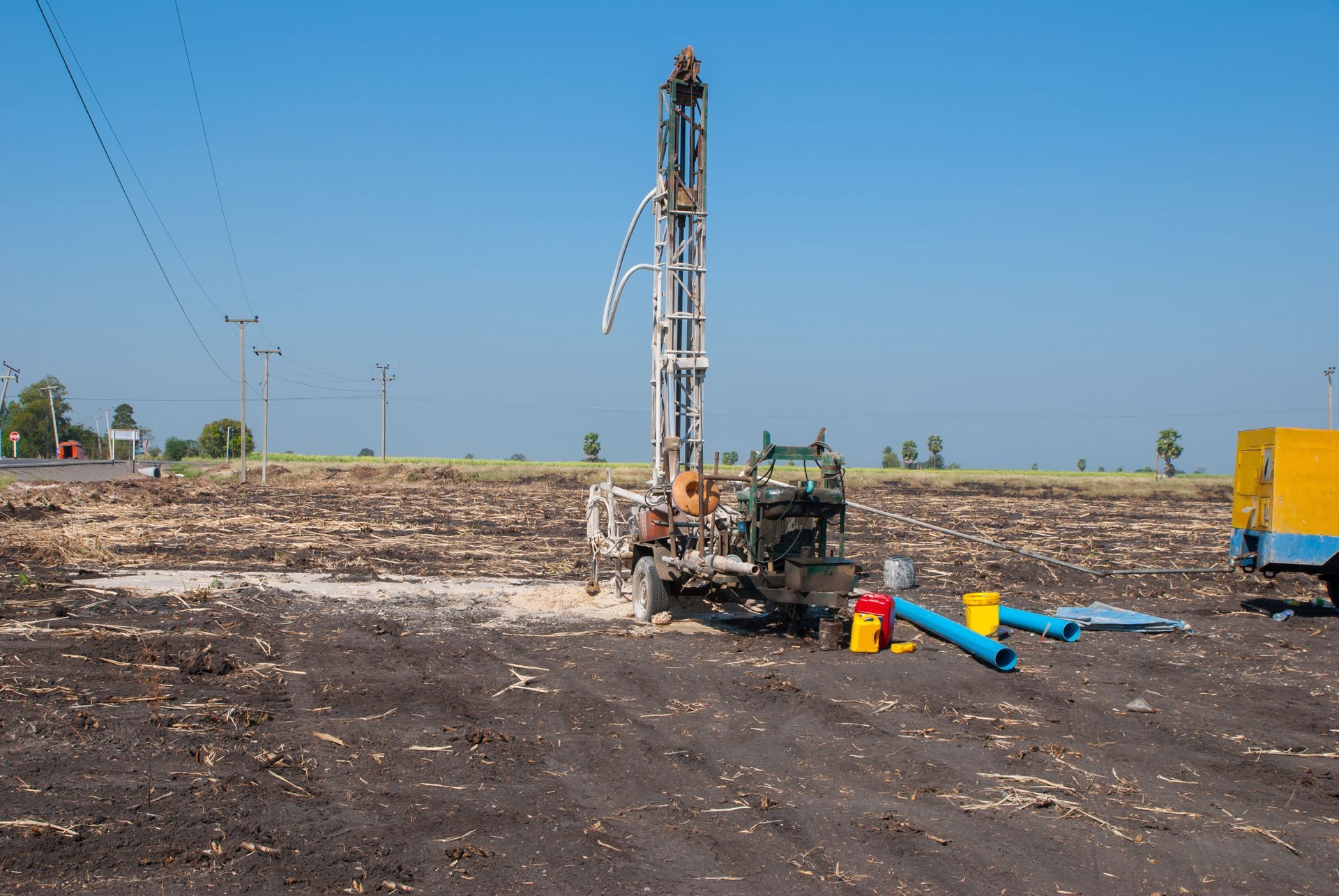 Drilling rig on a barren construction site under a clear blue sky, with pipes and equipment nearby