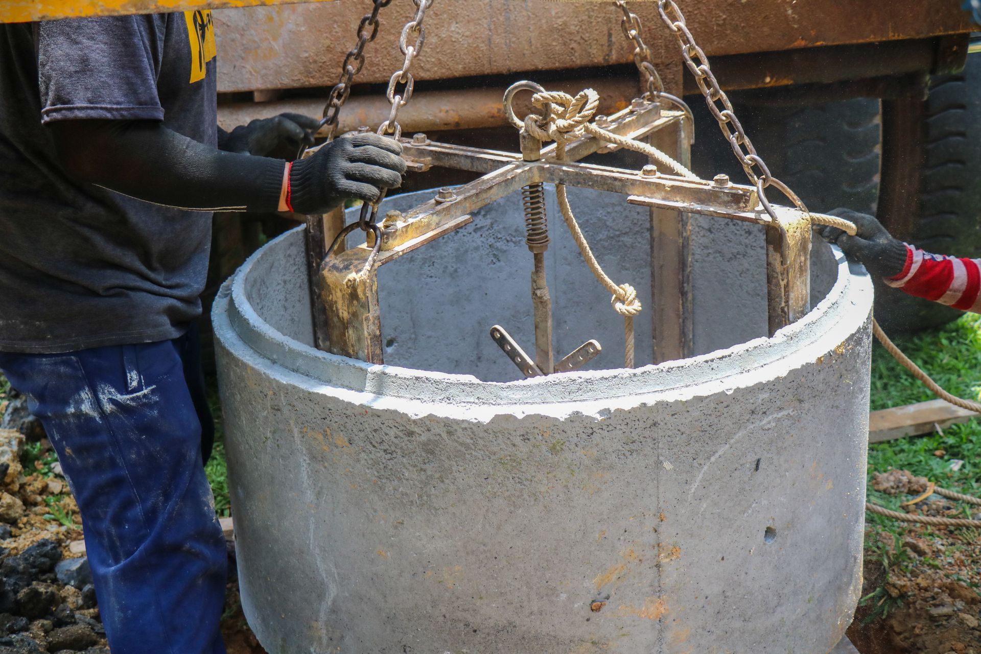 Worker lowering a metal frame into a concrete well shaft outdoors