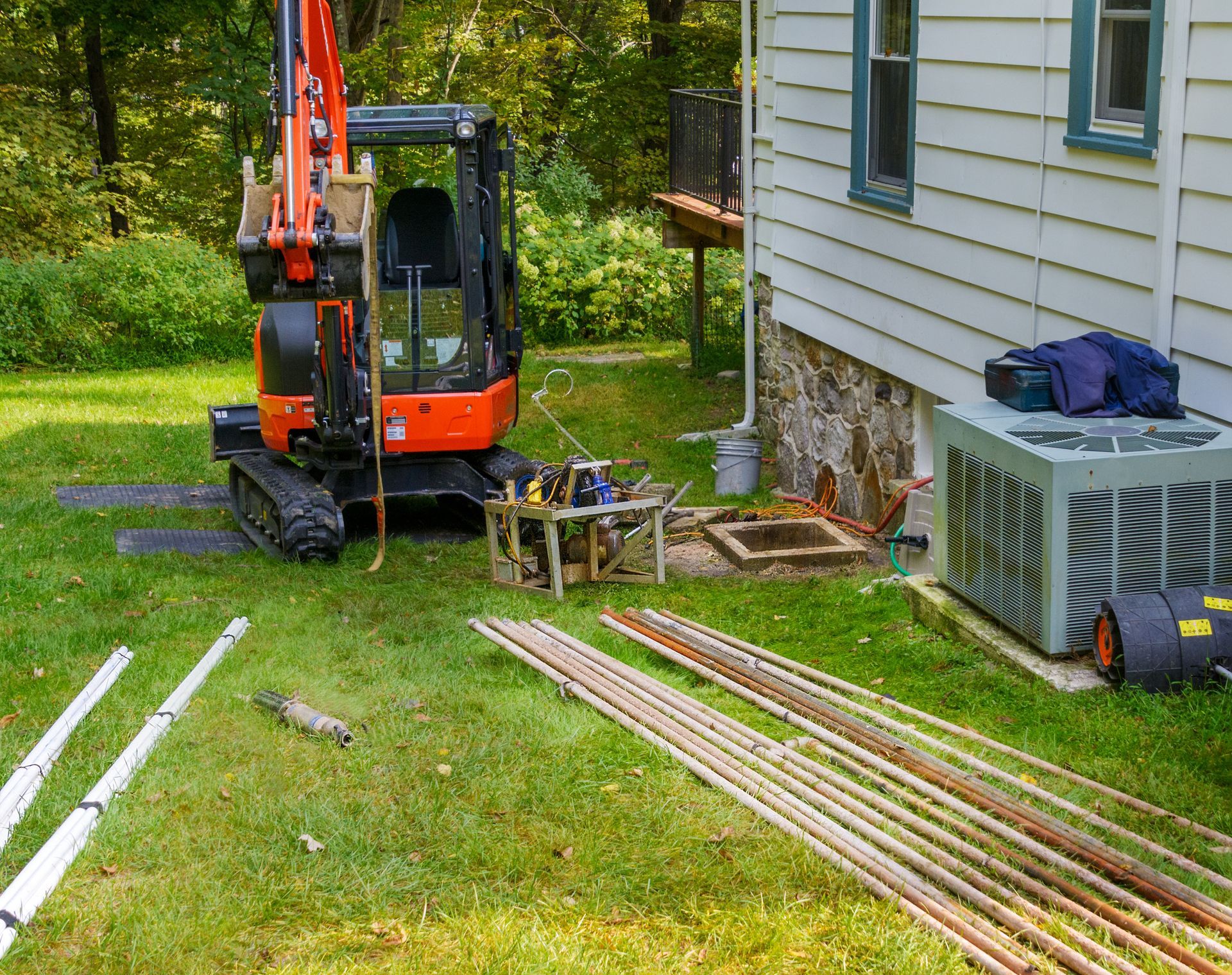 Compact excavator and construction materials on a lawn beside a house during outdoor work