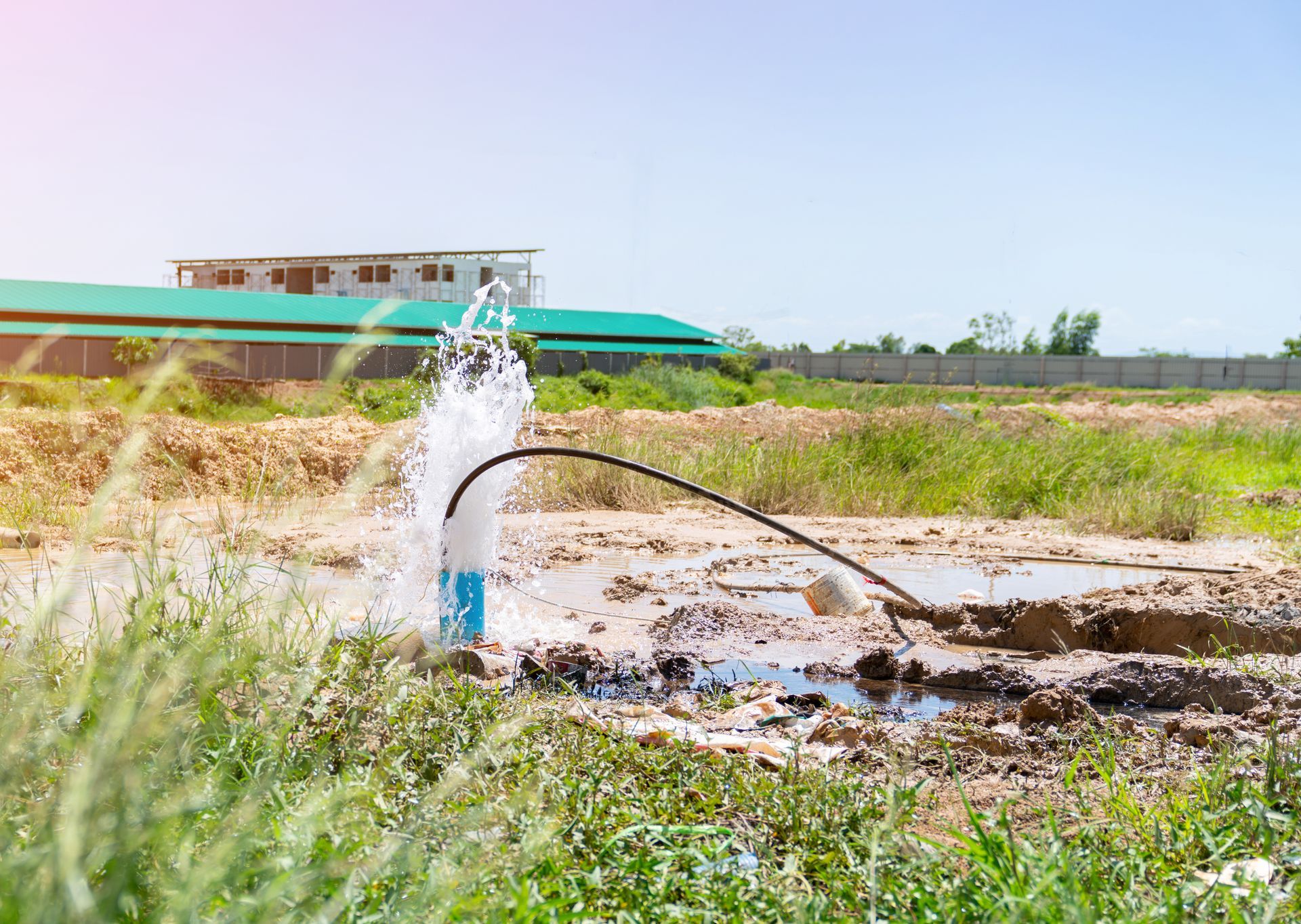 Water spraying from a broken pipe onto a dry field under a clear blue sky