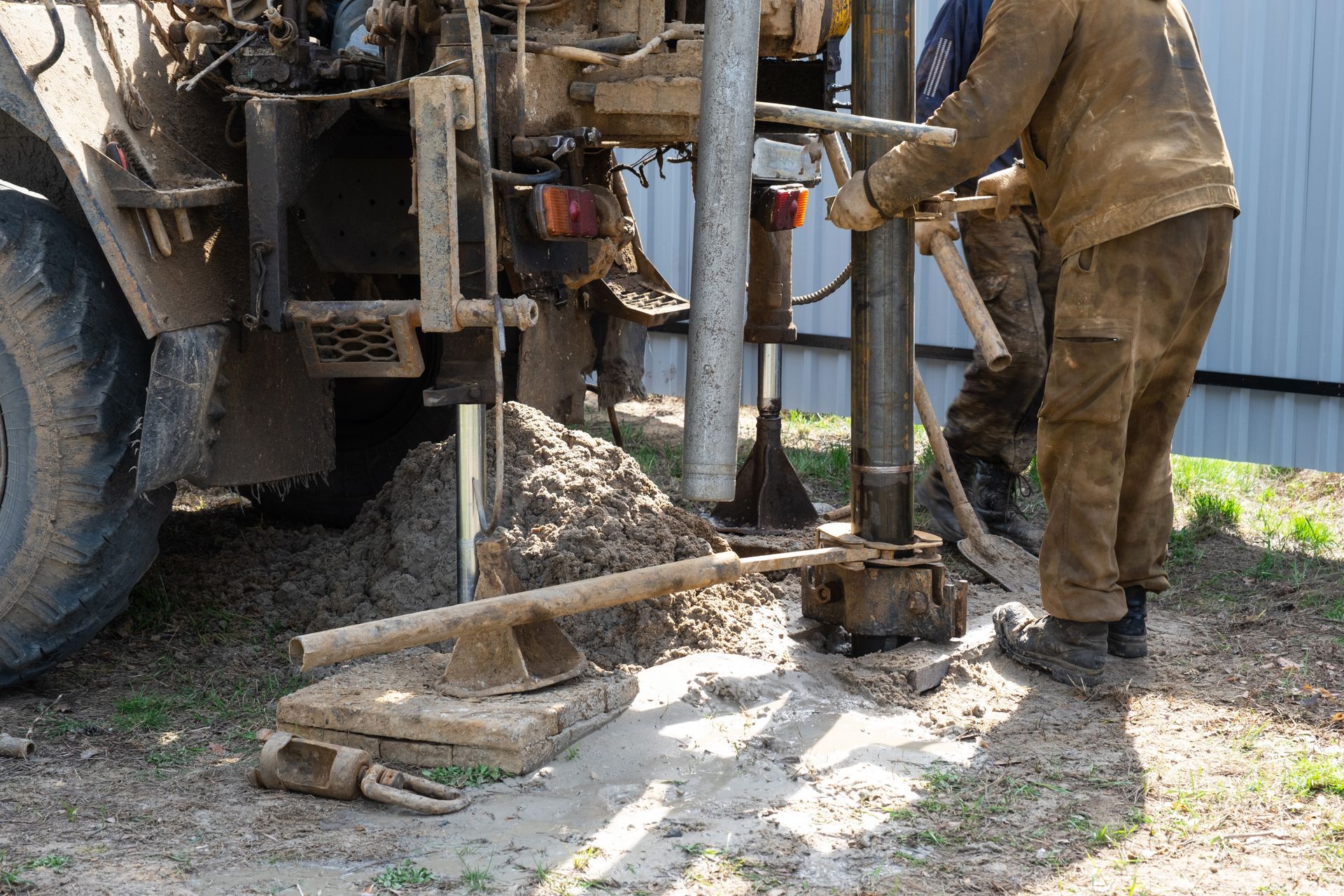 Worker operates drilling rig beside a truck on muddy ground
