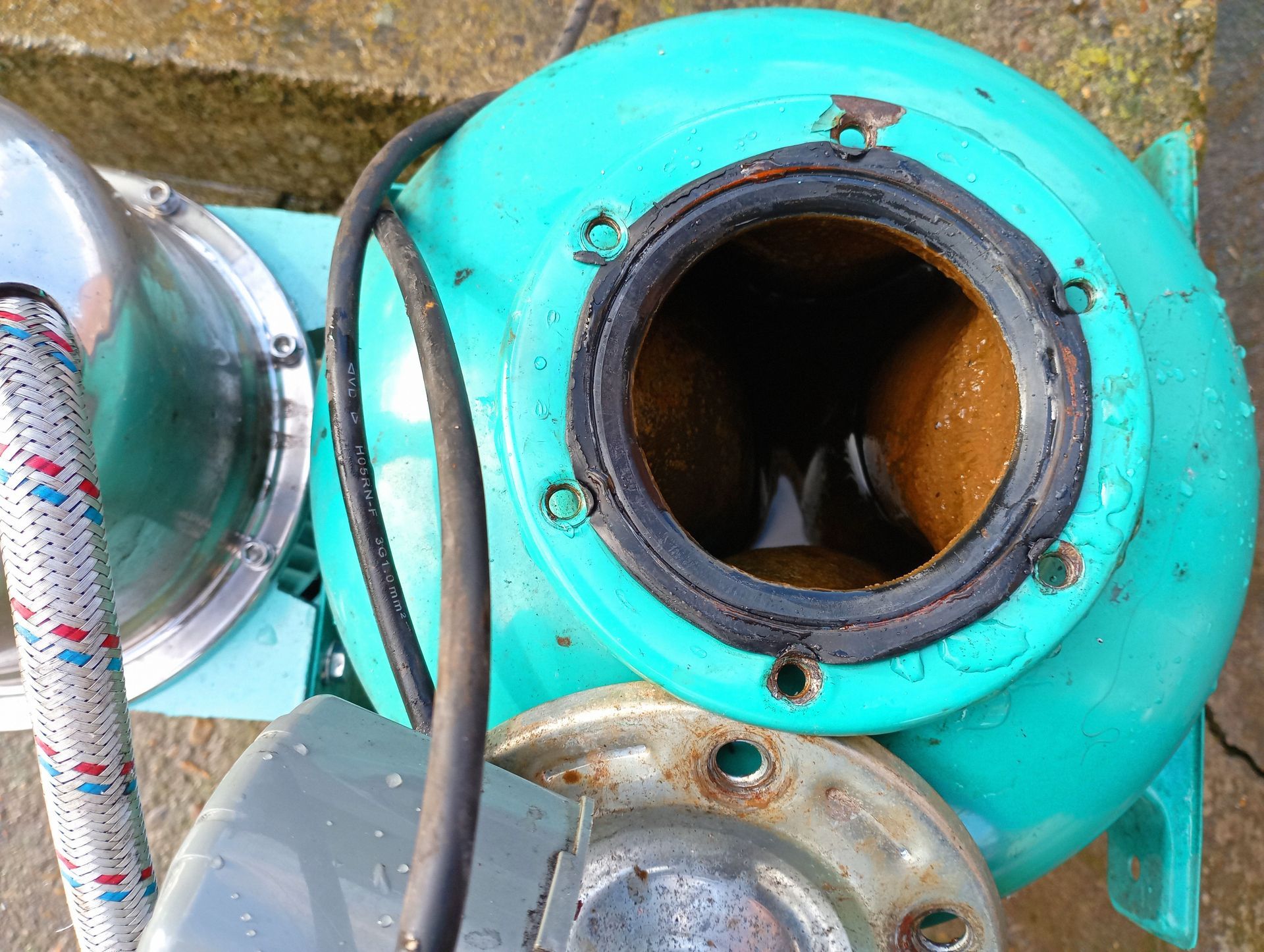 Turquoise mechanical pump with a circular opening and attached hoses on a stone surface