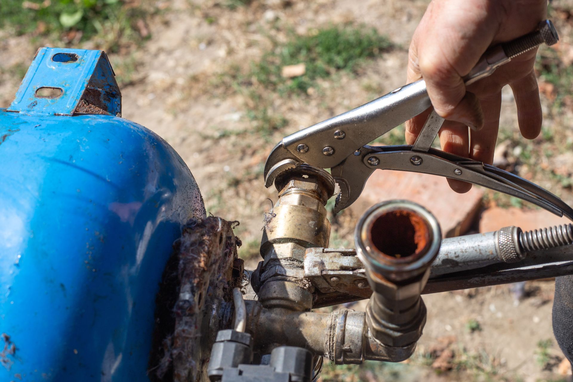 Hand using pliers to repair a valve on a blue metal tank outdoors