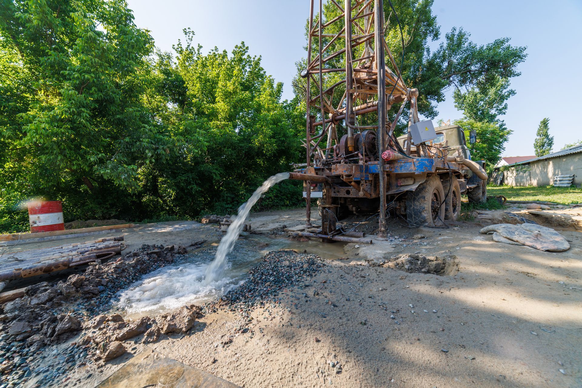 Drilling rig spraying water and mud at a roadside worksite with trees nearby
