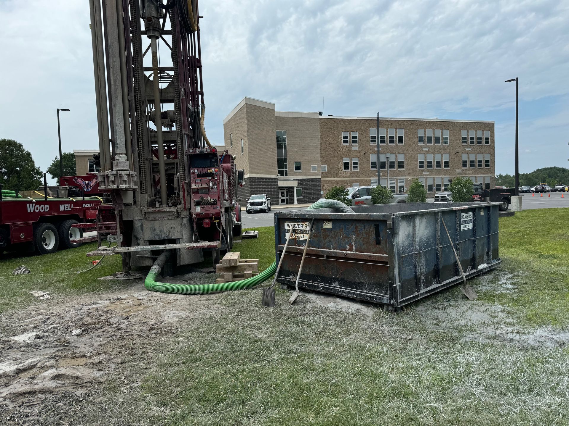 Drilling rig and yellow service truck on a barren site under a clear blue sky