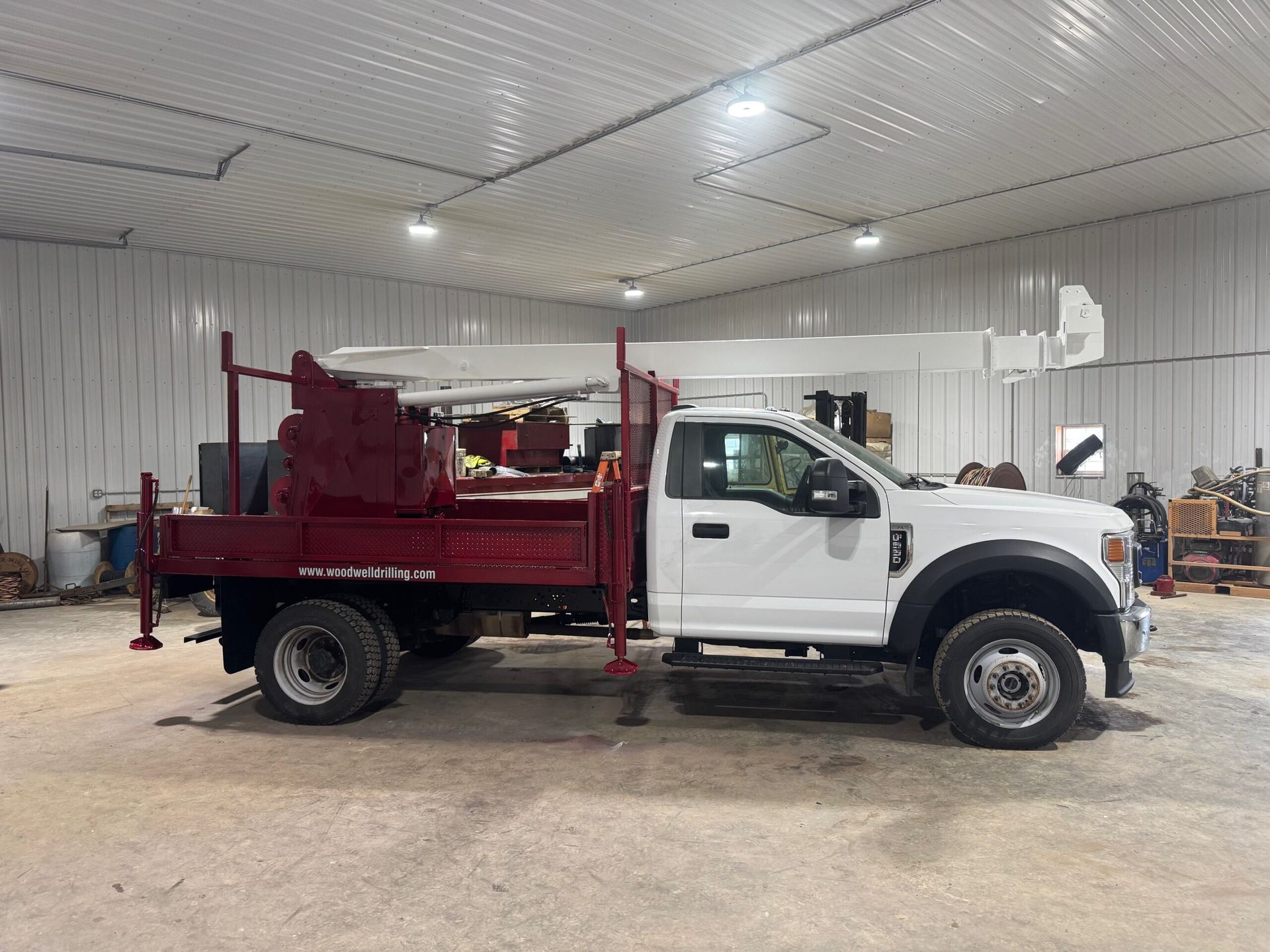 White flatbed truck with red equipment parked inside a workshop garage